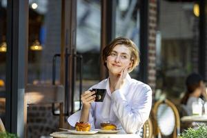 Caucasian woman sipping a hot espresso coffee while sitting outside the european style cafe bistro enjoying slow life with morning vibe at the city square with sweet pastry photo