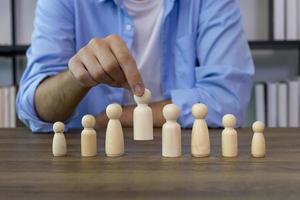 Manager hand pick the leader among the employee team using wooden figure for job recruitment, hiring and human resources management concept photo