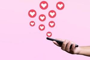 la gente usa el teléfono móvil para enviar corazones. concepto de amor y conexión usando la aplicación telefónica sobre fondo rosa. foto