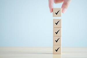 Checklist, Task list, Survey and assessment. Quality Control. Goals achievement and business success. Hand holding Check mark on wooden blocks for complete check list. photo