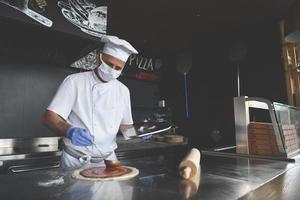 chef  with protective coronavirus face mask preparing pizza photo