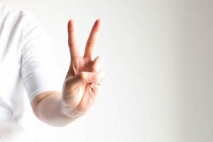 una mano que muestra el número dos levantando el dedo índice y el dedo medio en primer plano sobre fondo blanco y poca luz. foto