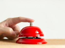 Close-up of index finger pressing the bell button of red vintage style handbell on wooden table. photo