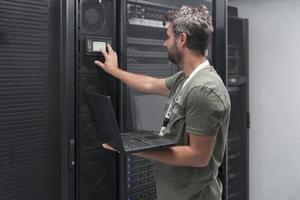 Data Center Engineer Using Laptop Computer Server Room Specialist Facility with Male System Administrator Working with Data Protection Network for Cyber Security or Cryptocurrency Mining Farm. photo