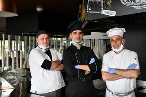 group chefs standing together in the kitchen at restaurant wearing protective medical mask and gloves in coronavirus new normal concept photo