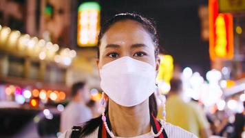 Portrait of a tourist woman wearing medical mask while standing on the street of city at night. photo