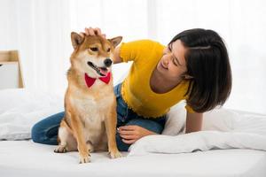 mujer feliz y perro shiba inu acostados juntos en una cama en casa foto