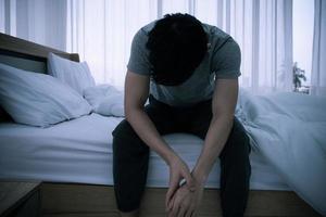 Stressed Asian young man sitting alone on bed. Bad relationship or bankrupt problem and sickness concept. photo
