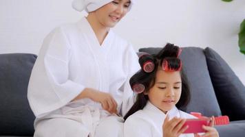 madre con hija pequeña en albornoces disfrutando del pelo rodante juntos en la sala de estar. foto