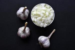 Garlic bulbs on a black background and a cup with chopped onions. Garlic and onion on a black background. photo