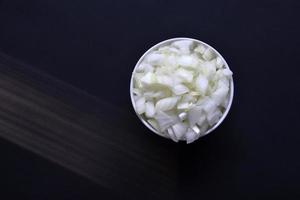 cebolla jugosa en un plato blanco sobre un fondo negro. deliciosa cebolla en rodajas en un bol. foto