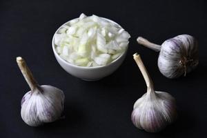 Garlic bulbs on a black background and a cup with chopped onions. Garlic and onion on a black background. photo