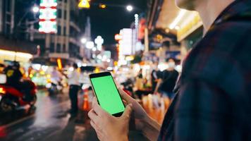 Female tourist holding smart phone with green screen display while standing on the street at night. photo