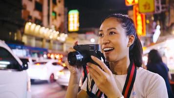 An Asian female tourist enjoys taking photos of the night view of Yaowarat Road or Chinatown in Bangkok, Thailand.