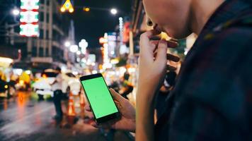 mujer turista sosteniendo un teléfono inteligente con pantalla verde mientras está de pie en la calle por la noche. foto