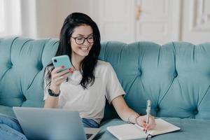 Female copywriter concentrated on remote job, prepares publication, watches webinar to improve skills, reads message, installs new application, uses free internet connection, smiles happily. photo
