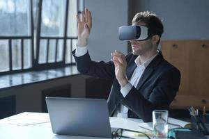Male office worker in vr headset interacting with digital interface while sitting at desk photo