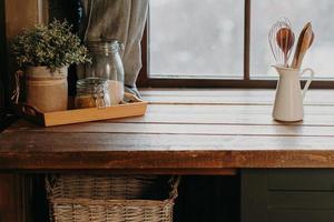 utensilios de cocina en un recipiente blanco sobre una mesa de madera cerca de la ventana. decoración de la cocina del hogar. batería de cocina. hora de cocinar. cubiertos en la habitación. foto