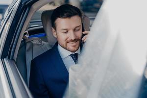 Businessman rides in black car in passenger seat and talking on cellphone photo