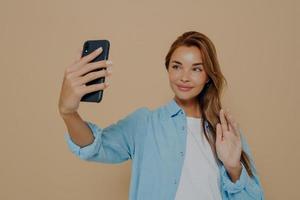 Cheerful lady waving at camera on beige background photo