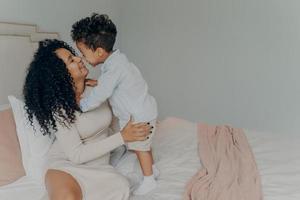 Happy pregnant mother embracing adorable little son while sitting on bed photo