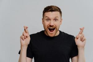 Young happy guy believer with open mouth crossing fingers for best luck photo