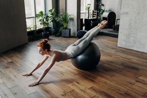 Slim woman balancing on stability exercise ball in fitness studio photo