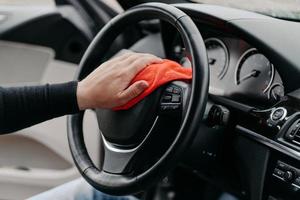 Close up shot of mans hand cleaning car steering wheel with microfiber cloth. Hygiene prevention during coronavirus outbreak photo