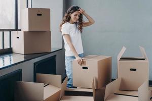 Tired woman unpacking cardboard boxes. Packing things, shipping service and relocation concept. photo