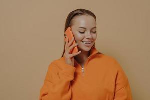 mujer joven feliz hablando por teléfono móvil con un amigo, disfrutando de una conversación telefónica, aislada en beige foto