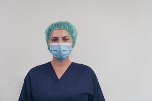 Close up of female doctor or scientist with a medical mask and surgical cap over grey background. She is adjusting mask with photo