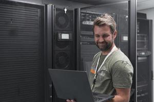 Data Center Engineer Using Laptop Computer Server Room Specialist Facility with Male System Administrator Working with Data Protection Network for Cyber Security or Cryptocurrency Mining Farm. photo