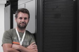 Portrait of male technician or network administrator standing brave as a hero with arms crossed in data center server room. photo