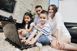 familia joven feliz divertirse y trabajar en la computadora portátil en casa foto