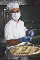 chef  with protective coronavirus face mask preparing pizza photo