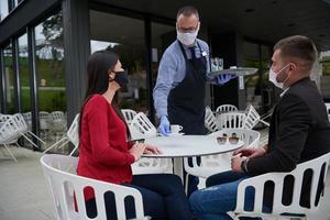 Waiter with protective medical mask and gloves serving guest photo