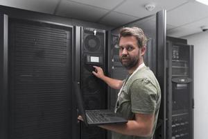 Data Center Engineer Using Laptop Computer Server Room Specialist Facility with Male System Administrator Working with Data Protection Network for Cyber Security or Cryptocurrency Mining Farm. photo