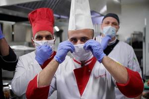 group chefs standing together in the kitchen at restaurant wearing protective medical mask and gloves in coronavirus new normal concept photo