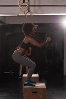 black female athlete is performing box jumps at gym photo