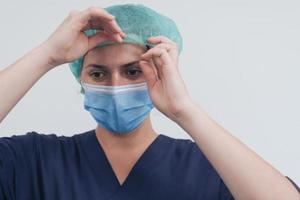 Close up of female doctor or scientist with a medical mask and surgical cap over grey background. She is adjusting mask with photo