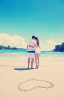 pareja romántica enamorada diviértete en la playa con el corazón dibujando en la arena foto
