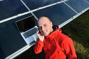 engineer using laptop at solar panels plant field photo