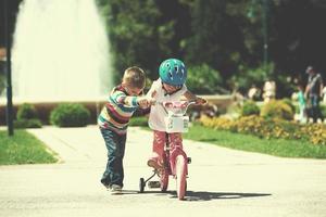 Boy and girl in park learning to ride a bike photo