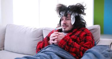 sick man is holding a cup while sitting on couch photo