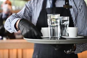 waiter in a medical protective mask serves  the coffee in restaurant photo