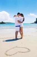una pareja feliz se divierte en la playa con el corazón en la arena foto