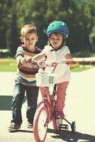 niño y niña en el parque aprendiendo a andar en bicicleta foto
