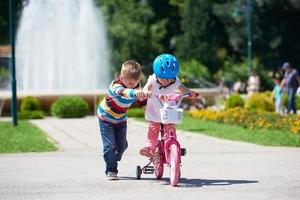 niño y niña en el parque aprendiendo a andar en bicicleta foto