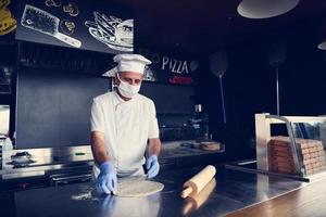 chef  with protective coronavirus face mask preparing pizza photo