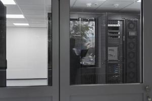 Software Engineer Working on a Laptop Computer in a Modern Server room. Monitoring Room Big Data Scientist in reflection of the entrance door. photo